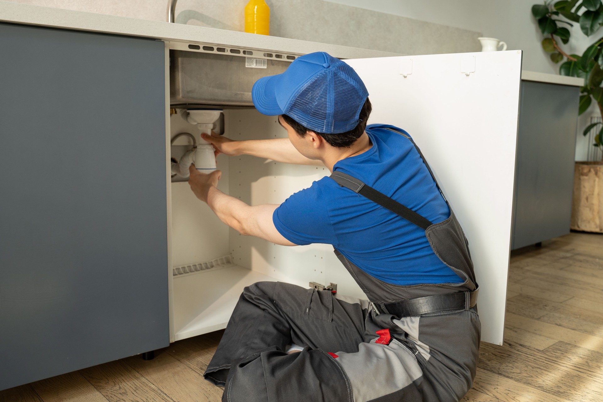 Professional Plumber Repairs Under-Sink Pipes in a Modern Kitchen